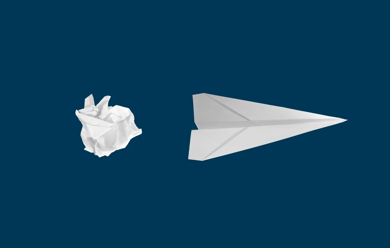 Crumpled paper and paper airplane on blue background.