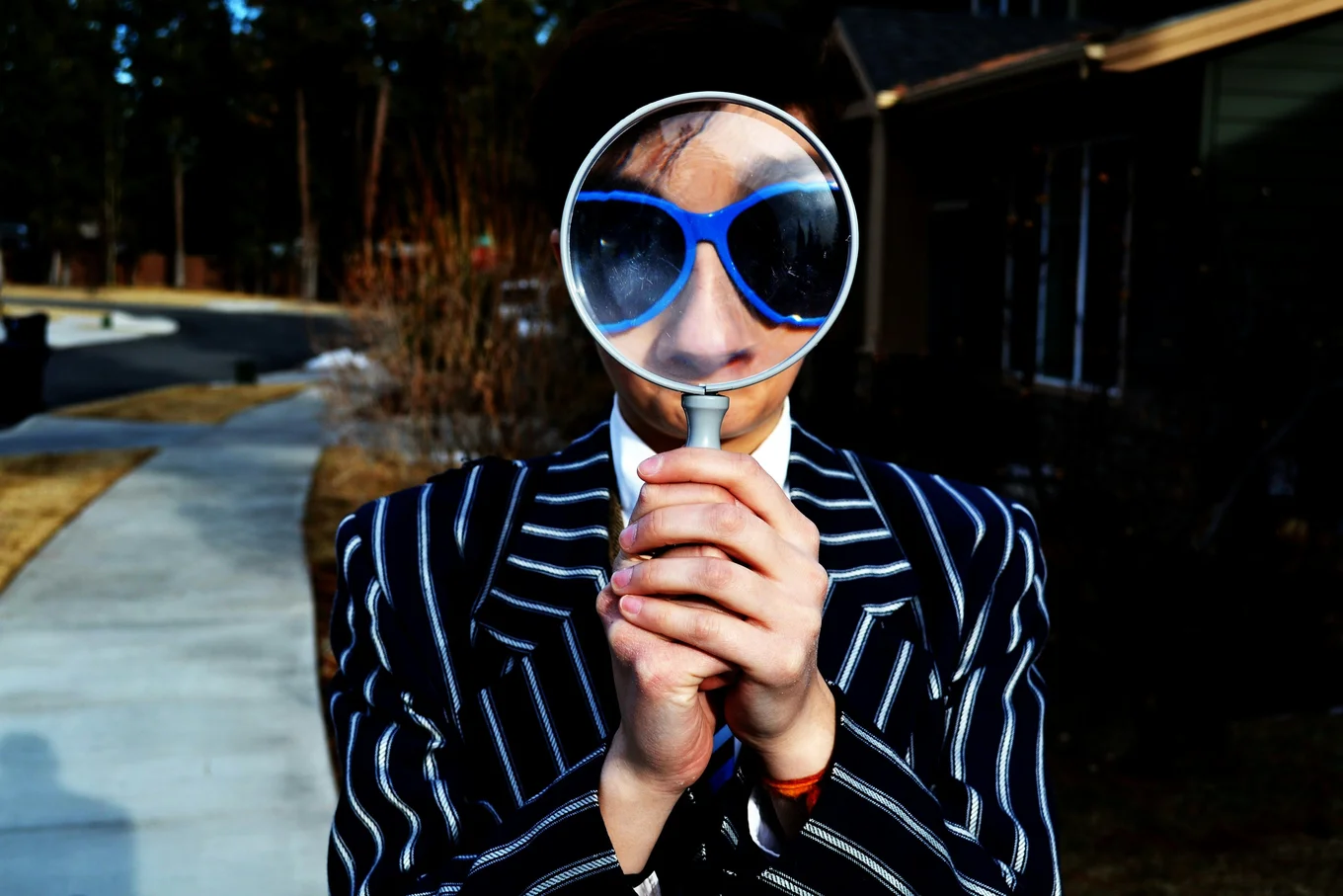 Person with magnifying glass, striped suit, outdoors.